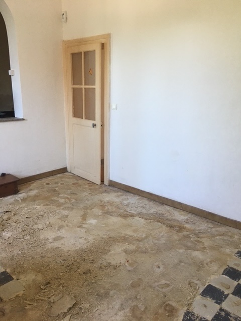 Le salon avant les travaux : sol nu et abîmé, murs blancs défraîchis, porte vitrée d'origine.
